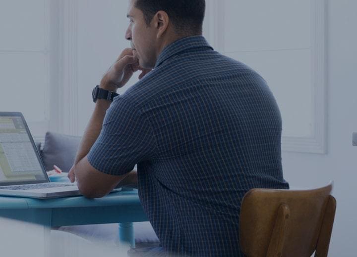 man sitting at a desk on his laptop with his hand on his chin