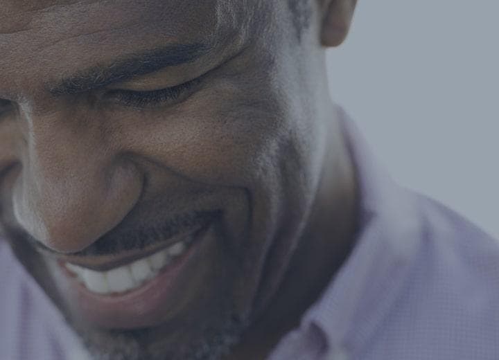 middle aged man in a purple shirt looking down and smiling