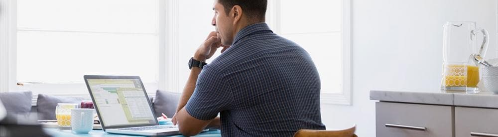 man sitting at a desk on his laptop with his hand on his chin